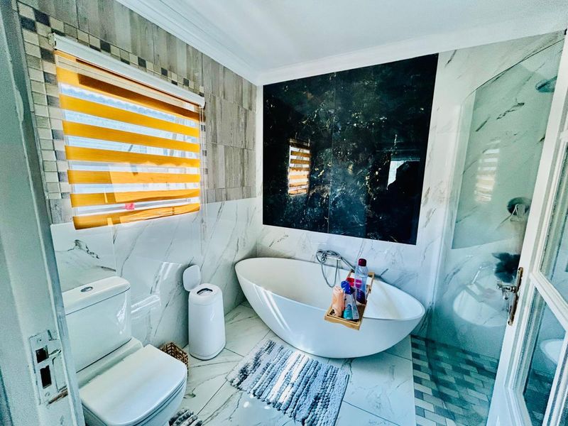 Modern bathroom featuring a sleek freestanding bathtub, marble-effect wall tiling, a striking dark feature wall, and a glass-enclosed shower area.