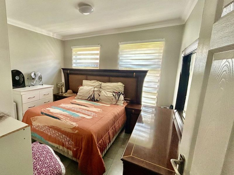 A functional bedroom featuring tiled flooring, neutral wall tones, and dual roller blinds for natural light control.