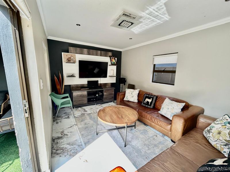 A well-lit living room featuring modern tiled flooring, a built-in media wall unit, and direct access to an outdoor patio area.