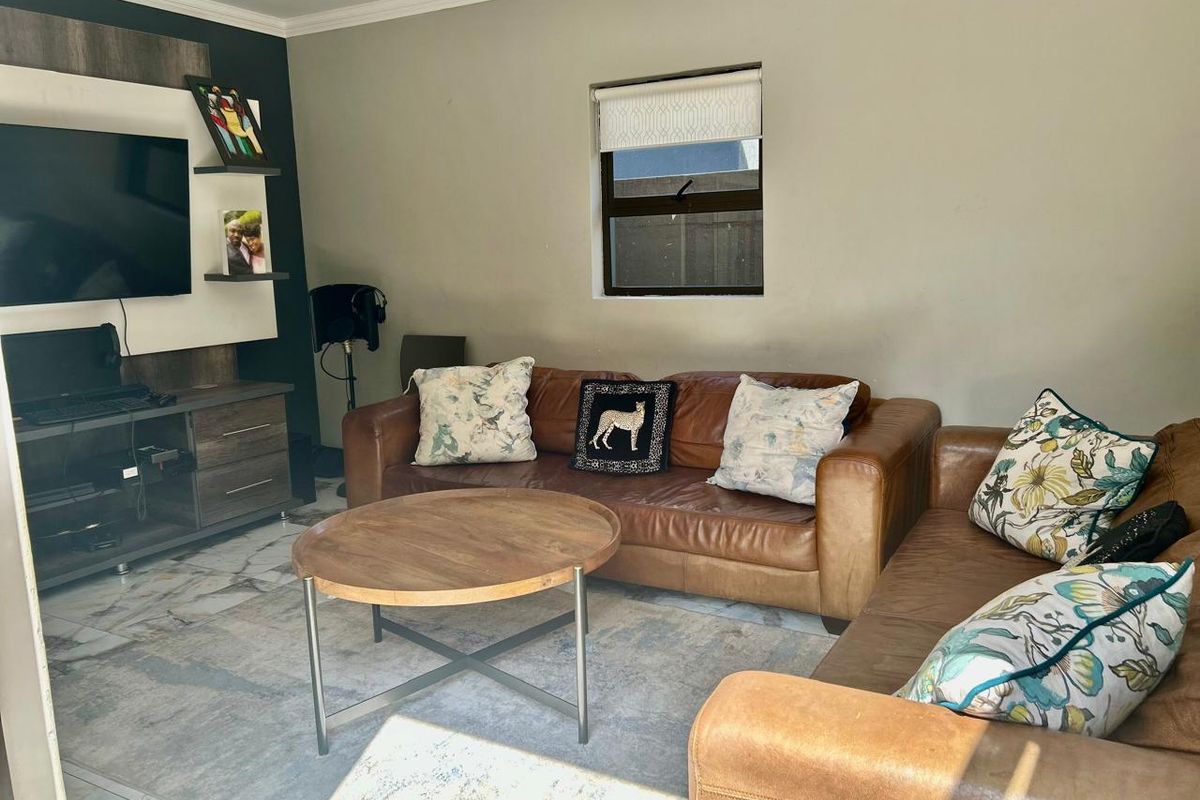A comfortable living room featuring tiled flooring, a built-in media unit, and a window with a roller blind.
