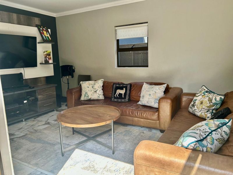 A comfortable living room featuring tiled flooring, a built-in media unit, and a window with a roller blind.
