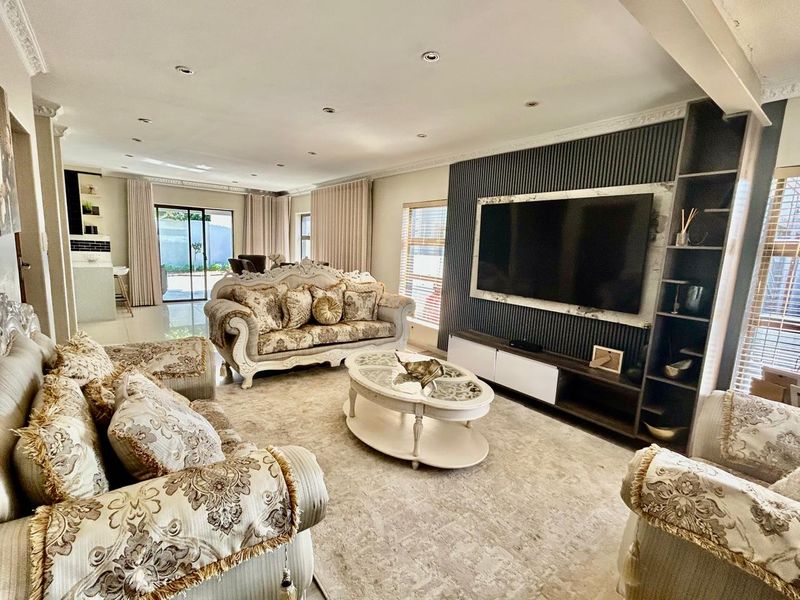 Spacious open-plan living area featuring a modern built-in media wall, recessed lighting, decorative cornicing, and seamless access to the outdoor patio through sliding glass doors.