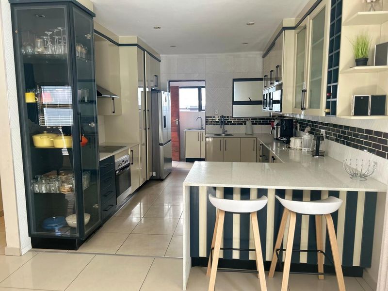 Modern kitchen featuring sleek cabinetry, stone countertops, integrated appliances, and a breakfast bar, with a functional layout and tiled flooring.