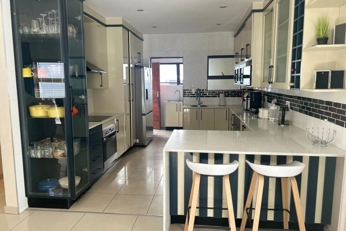 Modern kitchen featuring sleek cabinetry, stone countertops, integrated appliances, and a breakfast bar, with a functional layout and tiled flooring.
