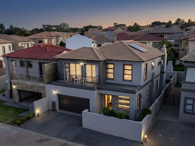 Aerial view of a modern two-story residential property featuring a tiled roof, solar panels, a balcony, and a paved driveway at dusk.