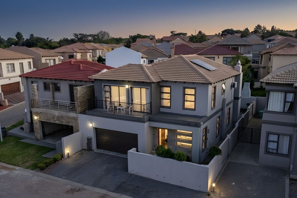 Aerial view of a modern two-story residential property featuring a tiled roof, solar panels, a balcony, and a paved driveway at dusk.
