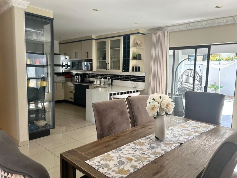 An open-plan kitchen and dining area featuring modern cabinetry, stone countertops, subway tile backsplash, and direct access to an outdoor patio through sliding glass doors.