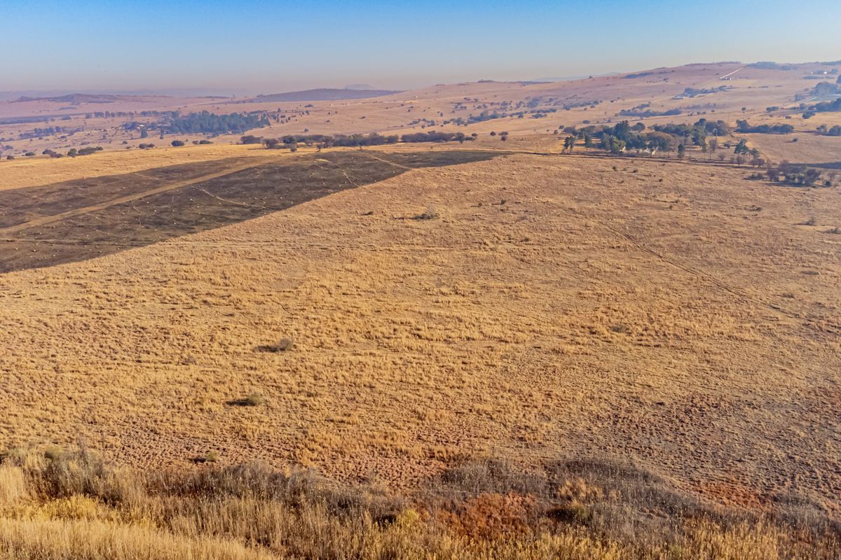 An aerial view of a large, open residential vacant land plot featuring dry grassland and rolling hills in the distance.