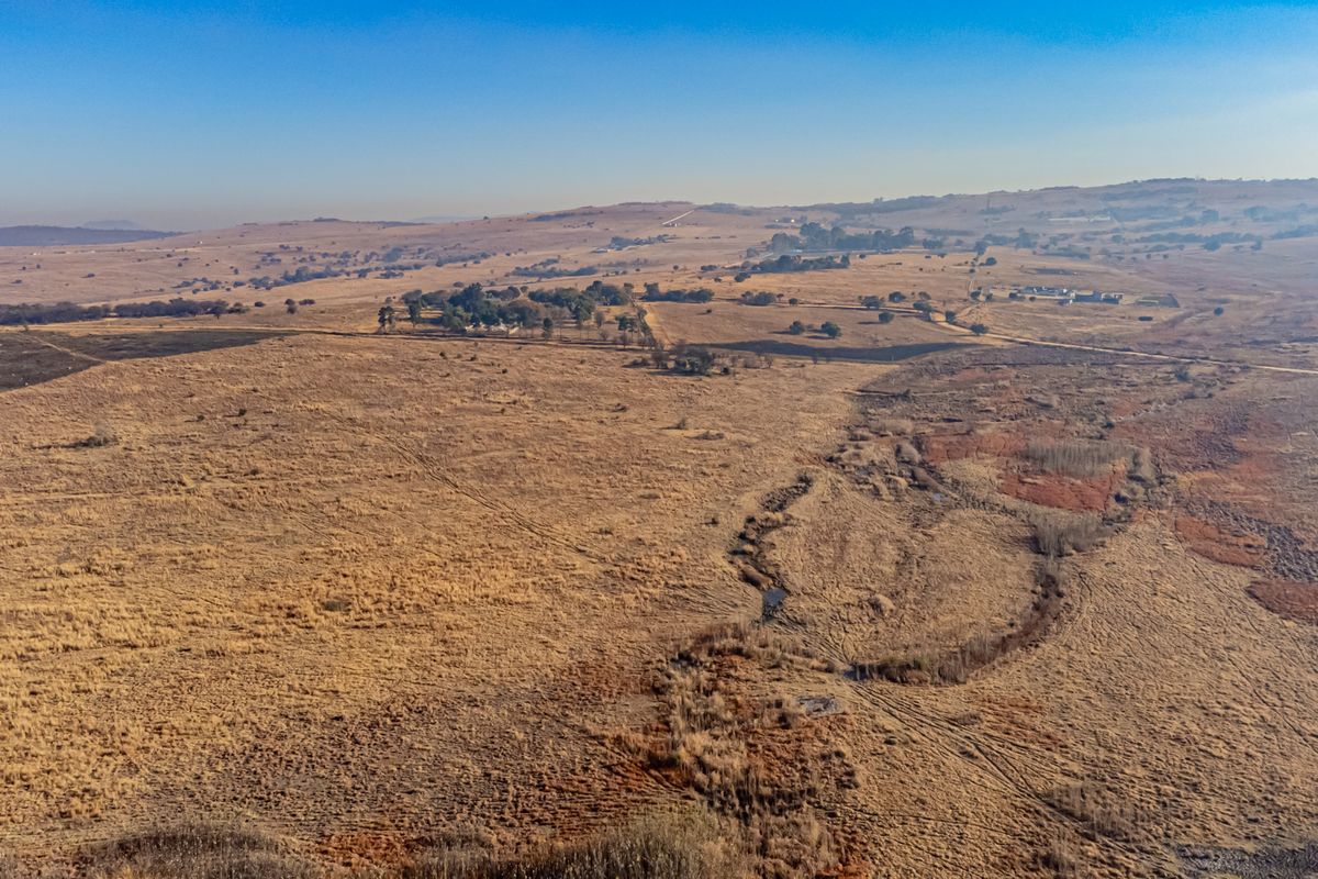 An expansive aerial view of open, undeveloped grassland featuring natural terrain and a winding watercourse, showcasing the property's vast landscape potential.