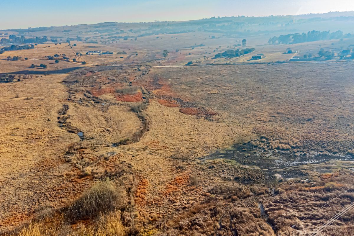 An aerial view of a large, open residential vacant land plot featuring natural grassland and a small watercourse.