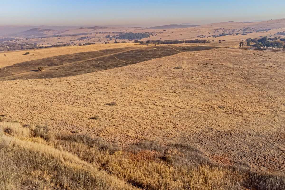 An aerial view of a large, open residential vacant land plot featuring dry grassland and rolling hills in the distance.
