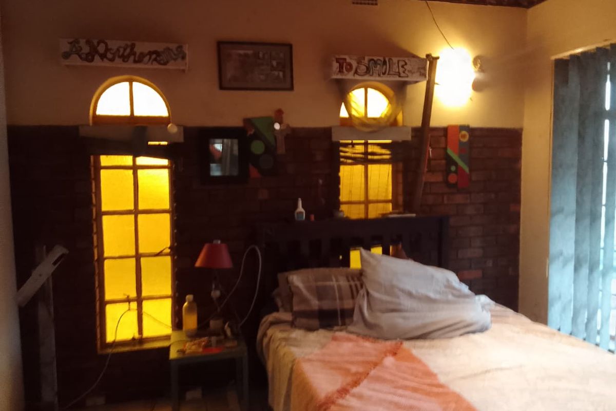 A bedroom featuring exposed brick walls, arched windows with yellow tinting, and vertical blinds, offering a unique but dated aesthetic.