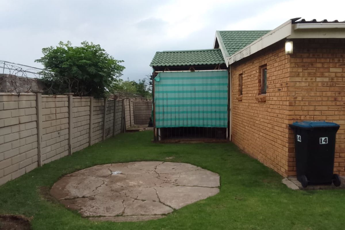 Rear exterior view of the property featuring a face brick facade, a small lawn area, and a cracked concrete patio slab.