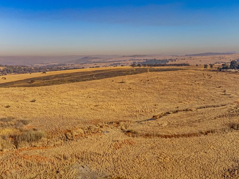 An aerial view of a large, open residential vacant land plot featuring natural grassland and expansive landscape views.