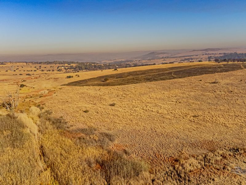 Aerial view of expansive vacant residential land featuring dry grassland, an unpaved access road, and visible high-voltage power line infrastructure.