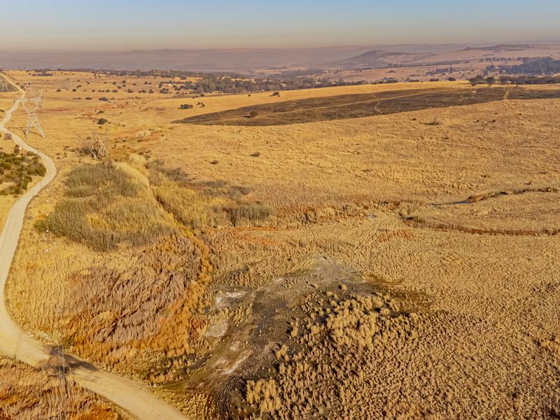 An aerial view of a large, undeveloped residential land parcel featuring natural dry grassland, a dirt access road, and visible power line infrastructure.
