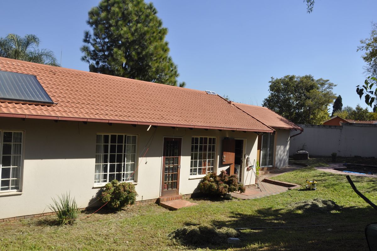 Rear view of the house featuring a tiled roof with solar water heating panels, brick patio area, and access to the garden.