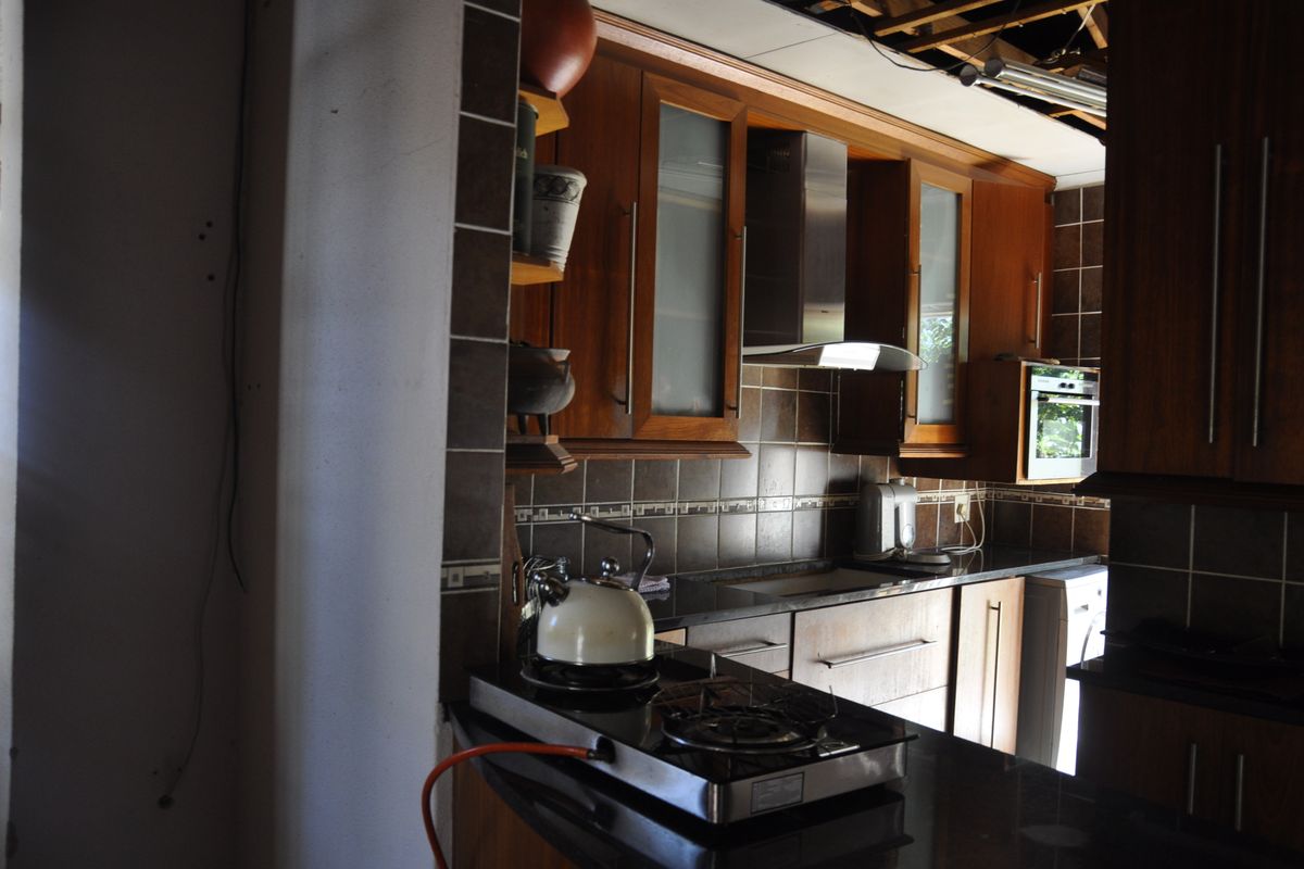 A kitchen featuring dark wood cabinetry, granite countertops, and a stainless steel extractor fan, currently undergoing renovation with exposed ceiling elements.