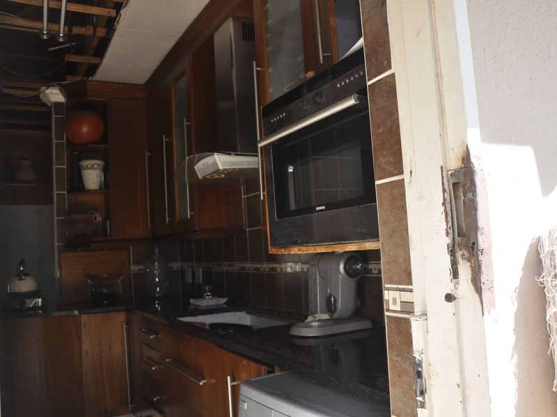 A dated kitchen featuring dark wood cabinetry, granite countertops, and built-in oven, currently showing significant signs of wear and structural ceiling damage.