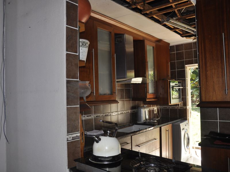 A kitchen featuring dark wood cabinetry, granite countertops, and tiled splashbacks, currently requiring significant ceiling repairs and maintenance.