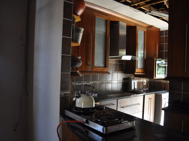 A kitchen featuring dark wood cabinetry, granite countertops, and a stainless steel extractor fan, currently undergoing renovation with exposed ceiling elements.