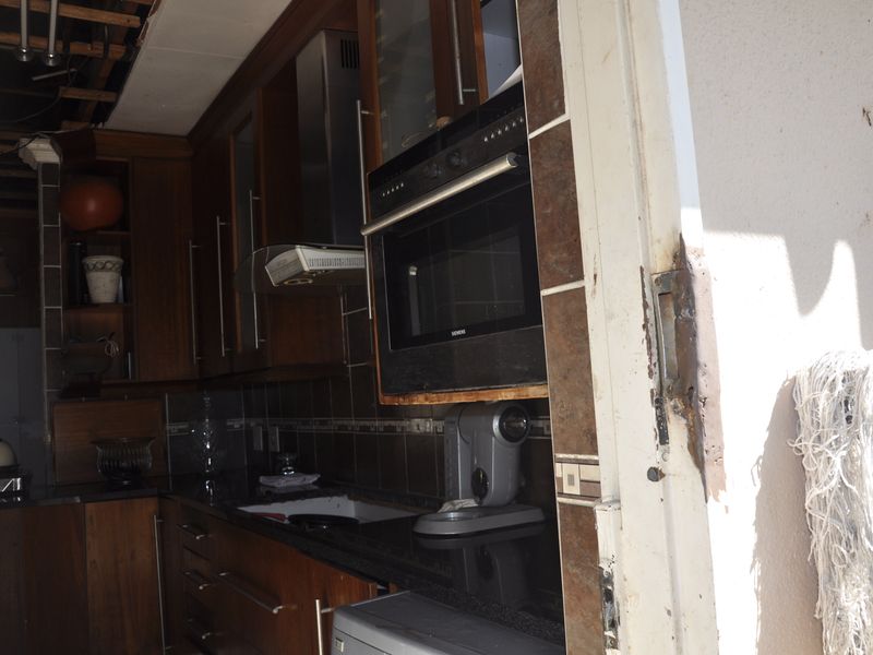 A kitchen featuring dark wood cabinetry, granite countertops, and built-in oven, currently showing significant signs of wear and structural damage to the ceiling.