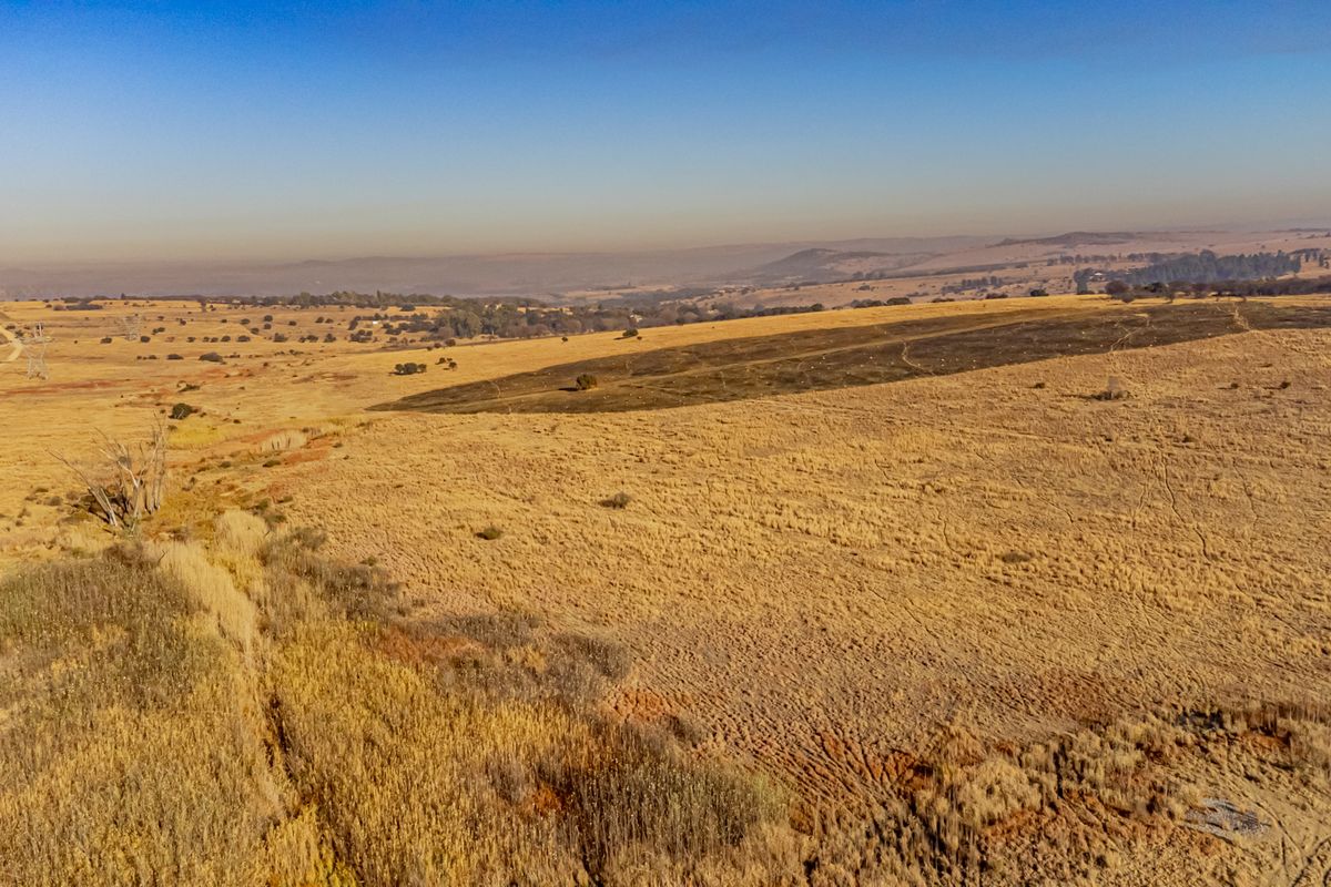 Aerial view of expansive vacant residential land featuring dry grassland, an unpaved access road, and visible high-voltage power line infrastructure.