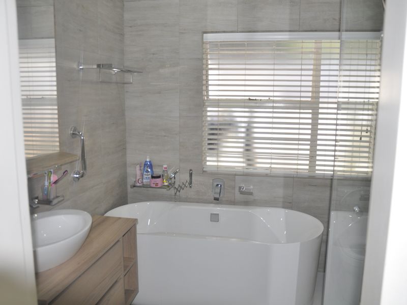 Modern bathroom featuring a freestanding bathtub, vessel sink with vanity cabinet, and a glass-enclosed shower with neutral wall tiling.
