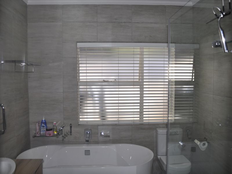 Modern bathroom featuring a freestanding bathtub, glass-enclosed shower, neutral wall tiling, and a window with fitted blinds.