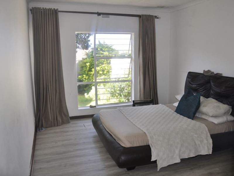 A bedroom featuring laminate flooring, a window with security bars, and visible ceiling water staining.
