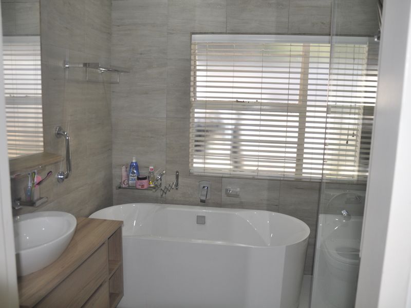 Modern bathroom featuring a freestanding bathtub, vessel sink with vanity cabinet, glass shower enclosure, and neutral wall tiling.