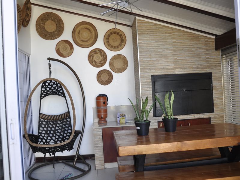 Covered patio area featuring a built-in braai with stone cladding, tiled flooring, and exposed beam ceiling, accessible via sliding doors.