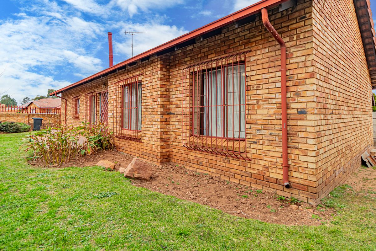 Rear view of a face brick house featuring security bars on windows, guttering, and a surrounding garden area.
