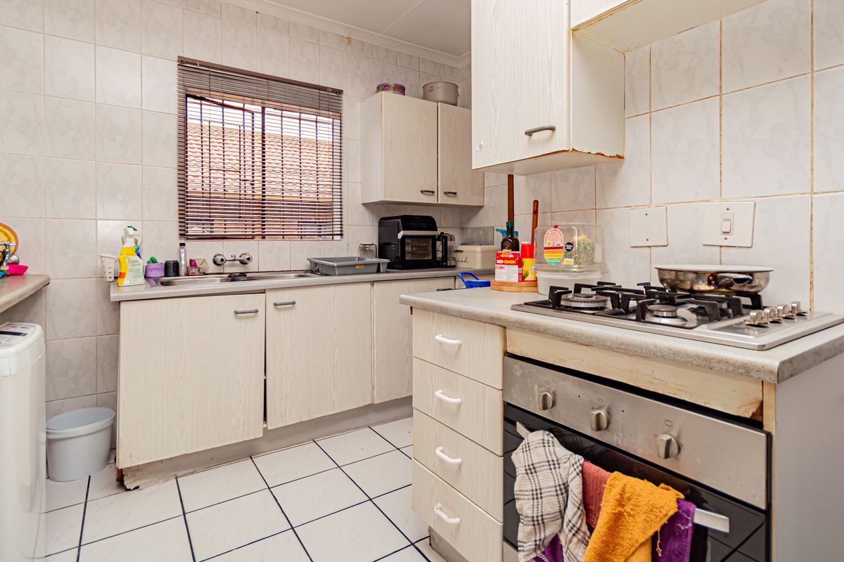 A functional kitchen featuring built-in cabinetry, a gas hob, an integrated oven, and tiled finishes, offering potential for modernization and cosmetic updates.
