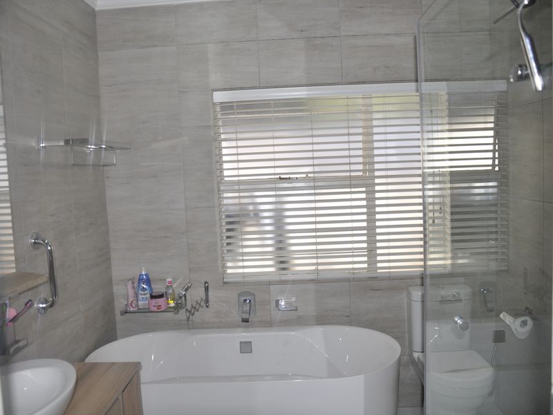 Modern bathroom featuring a freestanding bathtub, glass-enclosed shower, vanity basin, and neutral wall tiling with integrated chrome fixtures.
