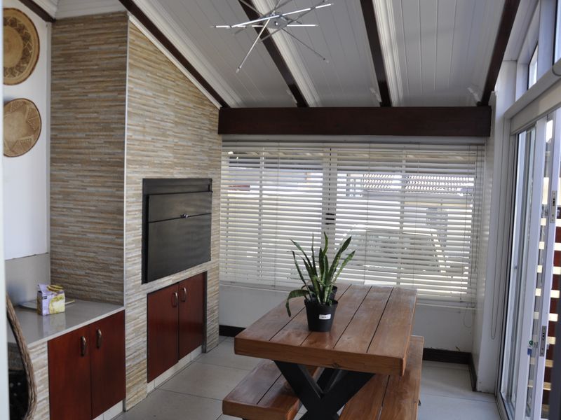 Enclosed patio area featuring a built-in braai, stone-clad feature wall, timber ceiling beams, and large sliding glass doors providing ample natural light.