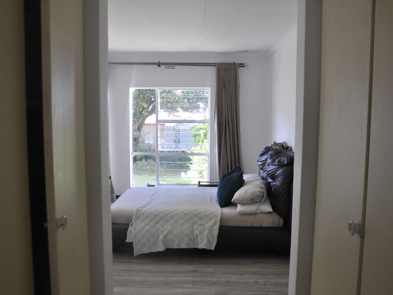 A bedroom featuring laminate flooring and a large window with security bars, showing signs of ceiling water damage and wear.