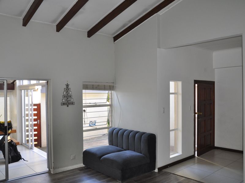 Living area featuring vaulted ceilings with exposed timber beams, tiled and laminate flooring, and direct access to an outdoor patio space.