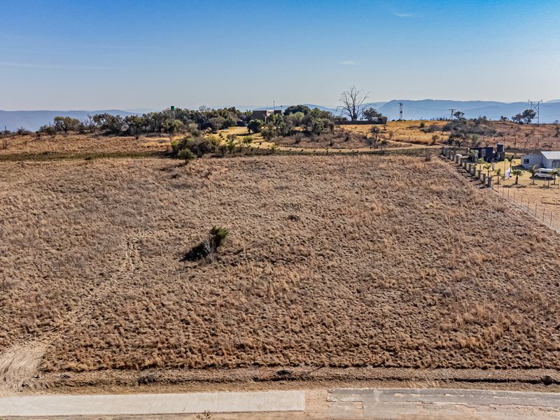 An aerial view of a large, vacant residential plot featuring dry grass and perimeter fencing in a rural landscape setting.