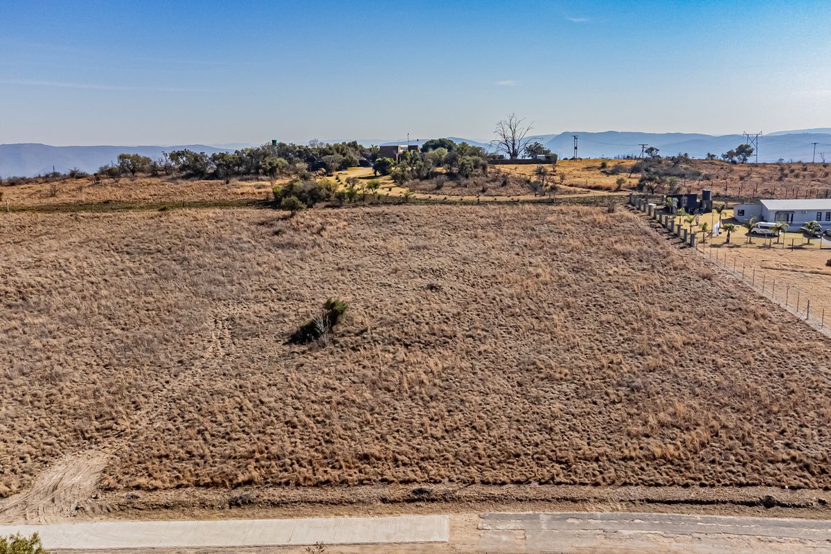 An aerial view of a large, vacant residential plot featuring dry grass and perimeter fencing in a rural landscape setting.