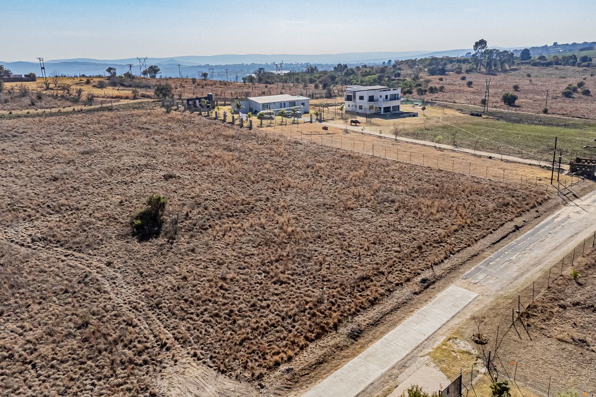 Aerial view of a vacant residential plot featuring perimeter fencing and adjacent paved road access in a developing rural area.