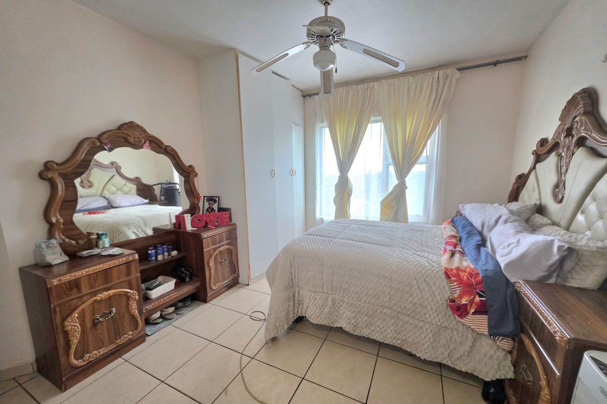 A bedroom featuring tiled flooring, a ceiling fan, and a built-in wardrobe, offering a functional space with natural light.