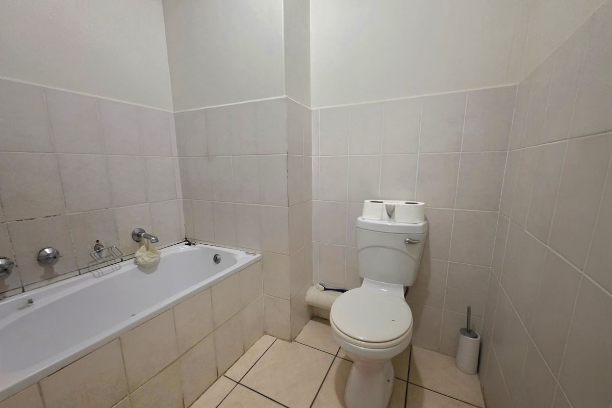 A functional bathroom featuring a standard bathtub, toilet, and neutral ceramic tiling throughout, offering a clean canvas for potential cosmetic updates.