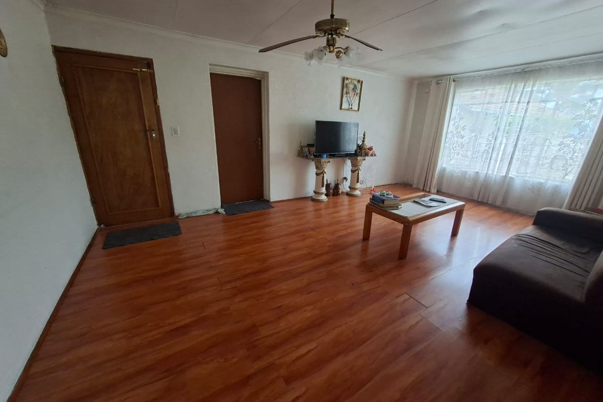 A living room featuring wood-look laminate flooring, a ceiling fan, and two wooden doors, providing a functional and neutral living space.