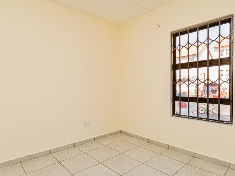 A clean, empty bedroom featuring neutral tiled flooring and a window fitted with security bars.