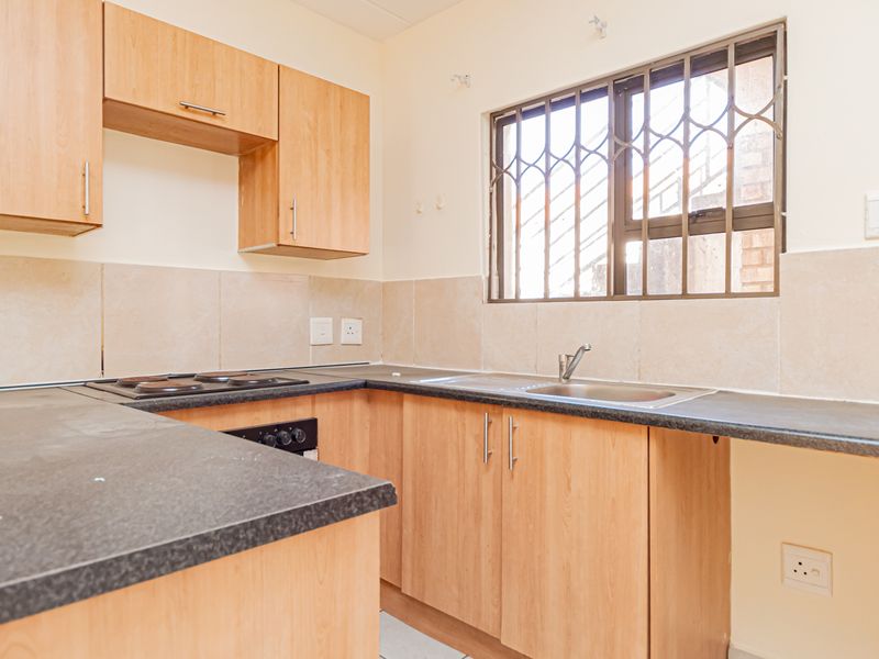 A functional kitchen featuring light wood-finish cabinetry, dark laminate countertops, a built-in electric hob and oven, and a stainless steel sink.