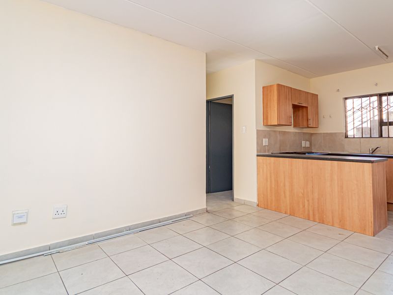 An open-plan living and kitchen area featuring tiled flooring, built-in wooden cabinetry, and a functional kitchen layout with a tiled backsplash.