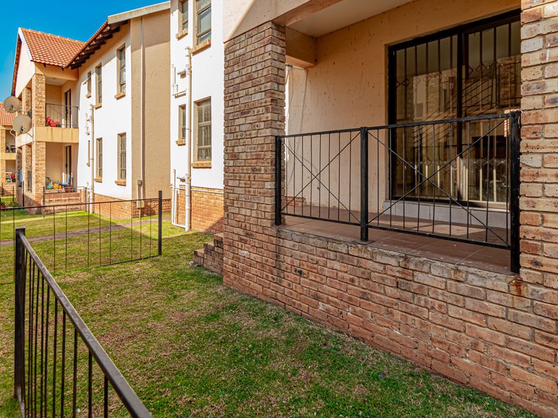 Rear view of an apartment complex featuring a ground floor patio with brick pillars, metal security gate, and a small private lawn area.
