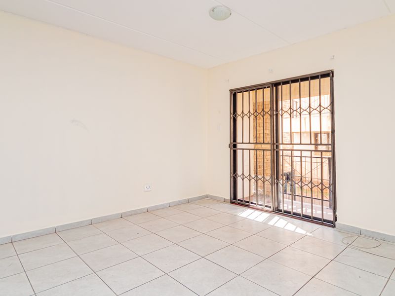 An empty living room featuring neutral tiled flooring and a sliding glass door with a security gate leading to an outdoor area.