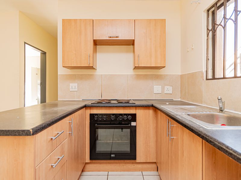 A functional kitchen featuring light wood cabinetry, dark laminate countertops, a built-in oven with hob, and a stainless steel sink with tiled backsplash.